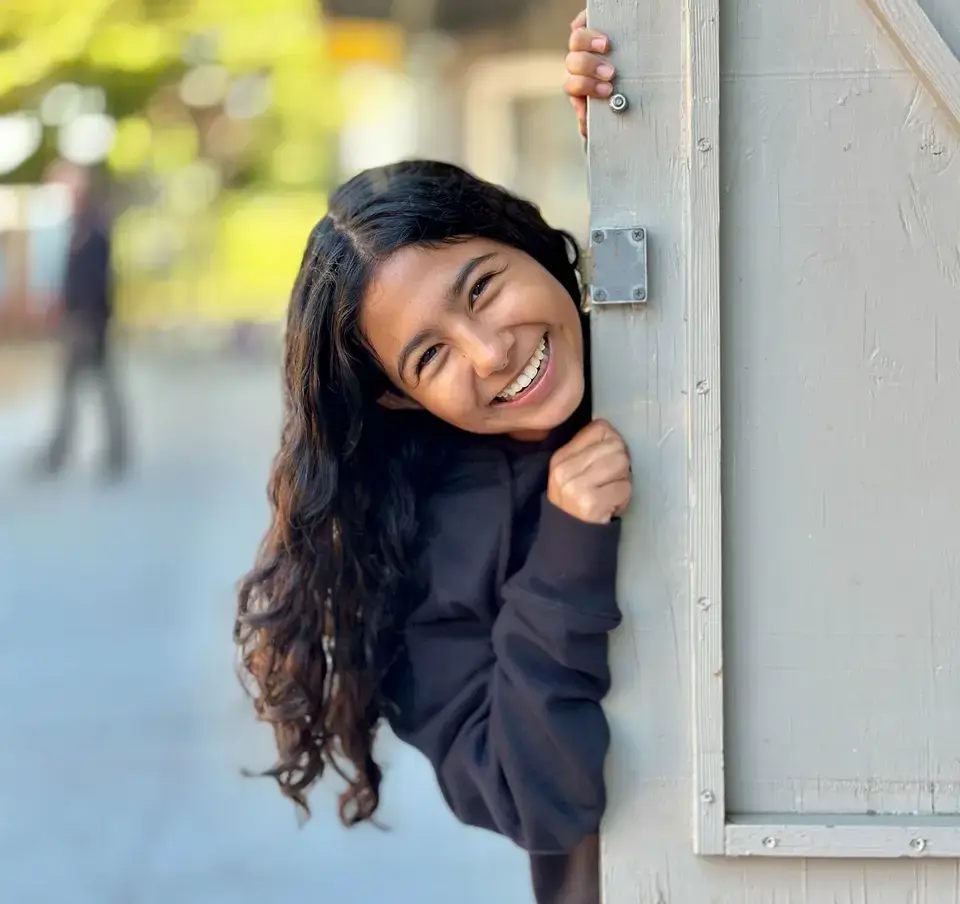 Girl_smiling_and_peering_from_behind_door